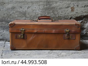 Old leather suitcase resting against a textured wall. Стоковое AI-изображение, AI-художник Иван Рябоконь / Фотобанк Лори