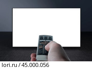 Television on gray wall and remote control in hand. Watching online TV. TV 8K flat screen oled with White blank screen. TV mockup. Стоковое фото, фотограф Павел Муравьев / Фотобанк Лори