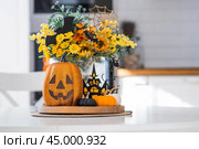 A vase of flowers, pumpkins and a scary castle with a witch on the background of a Scandi-style white kitchen interior. The concept of home and comfort. Autumn decor for Halloween. Стоковое фото, фотограф Photojuli / Фотобанк Лори