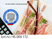 Время платить налоги. Налоговое уведомление, деньги, калькулятор, очки и эмблема Федеральной налоговой службы.  Крупный план. Стоковое фото, фотограф Лариса Гордеева / Фотобанк Лори