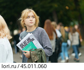 Moscow, Russia - September 5, 2019: Portrait of young woman with a newspaper visiting the city festival in the Gorky park. A crowd of youth around her. Blurred background. Редакционное фото, фотограф YuryKara / Фотобанк Лори