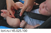 Close-up of an infant securely fastened in a car seat. Mum's hands fasten the seat belt over the baby's legs, ensuring the car seat is properly secured. The baby is calm. Стоковое видео, видеограф Воловодов Владимир / Фотобанк Лори