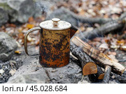 Old sooty coffee pot warming on campfire embers after rain. Стоковое AI-изображение, AI-художник Иван Рябоконь / Фотобанк Лори