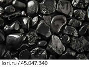 Polished black obsidian tumbled stones forming a mysterious background. Стоковое AI-изображение, AI-художник Иван Рябоконь / Фотобанк Лори