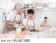 Elderly woman assisting adult son painting ceramic mugs in family workshop. Стоковое фото, фотограф Яков Филимонов / Фотобанк Лори