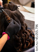 Hairstylist making curly hair for hairstyle brunette woman in barber shop. Close-up of hairdresser hands curling using black iron in salon. Customer service at hair salon, haircare. Copy ad text space. Стоковое фото, фотограф Aleksandr Golubev / Фотобанк Лори