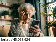 Fraud and deception. A shocked, worried elderly woman looking at her smartphone with unpleasant surprise, experiencing stress, financial problems, money theft. Стоковое AI-изображение, AI-художник Photojuli / Фотобанк Лори