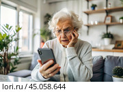 Fraud and deception. A shocked, worried elderly woman looking at her smartphone with unpleasant surprise, experiencing stress, financial problems, money theft. Стоковое AI-изображение, AI-художник Photojuli / Фотобанк Лори