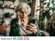 Fraud and deception. A shocked, worried elderly woman looking at her smartphone with unpleasant surprise, experiencing stress, financial problems, money theft. Стоковое AI-изображение, AI-художник Photojuli / Фотобанк Лори