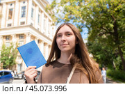 Девочка-подросток или молодая женщина держит в руках российский аттестат об окончании школы, стоит перед зданием университета, собирается подавать документы в вуз. Стоковое фото, фотограф Яна Проничева / Фотобанк Лори