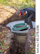 A worker installs a sewer manhole on a septic tank made of concrete rings. Construction of sewage disposal systems for private houses. Стоковое фото, фотограф Коханова Наталья / Фотобанк Лори