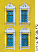 Front view on a facade of ancient yellow building with four windows with carved white stone platbands  as texture (vertical orientation) (2018 год). Стоковое фото, фотограф Михаил Строгалев / Фотобанк Лори