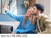 Happy young couple takes a selfie together with smartphone on sofa at home. Стоковое фото, фотограф Raquel Corcoles Mendez / Фотобанк Лори