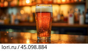 Chilled pint of beer on wooden bar surface, effervescent bubbles rising to creamy foam top, out-of-focus liquor shelf backdrop in cozy tavern atmosphere. Стоковое AI-изображение, AI-художник Павел Муравьев / Фотобанк Лори