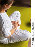 Woman doing kundalini yoga, meditating sitting in lotus position with hands folded dhyana mudra gesture, training on mat in room. Стоковое фото, фотограф Сергей Чайко / Фотобанк Лори