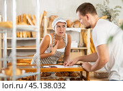In bakery, male visitor and female salesperson work with paper documents and count using phone. Стоковое фото, фотограф Яков Филимонов / Фотобанк Лори