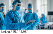 Healthcare professionals in protective gear monitor patient health in a modern clinic during daytime. Стоковое AI-изображение, AI-художник Сергей Толмачёв / Фотобанк Лори