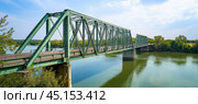 Old green metal truss bridge spanning a wide river. Стоковое AI-изображение, AI-художник Юрий Поздников / Фотобанк Лори