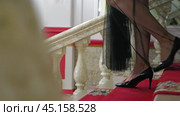 A close-up of a woman's slender legs in black high-heeled shoes gracefully descending a red-carpeted staircase. The staircase is decorated with ornate marble handrails. Side view. Стоковое видео, видеограф Воловодов Владимир / Фотобанк Лори