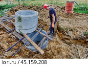 Installation of septic tank made of concrete rings for suburban sewerage system, worker pushes rings one over other. Стоковое фото, фотограф Владимир Григорьев / Фотобанк Лори