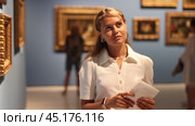 Young girl holding an information booklet looks at paintings in an art exhibition in a museum. Стоковое видео, видеограф Яков Филимонов / Фотобанк Лори