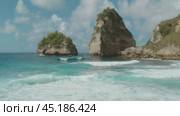 Clear blue waves crash against the towering cliffs covered with lush vegetation, creating a serene natural seascape. Стоковое видео, видеограф Igor Tichonow / Фотобанк Лори