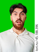 Surprised young man with a beard expressing shock against a bright green background. Стоковое фото, фотограф Сергей Толмачёв / Фотобанк Лори