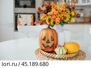 A vase of flowers,a jack pumpkin and candles on a tray. In the background - the interior of a white kitchen in Scandi style. The concept of home and comfort. Autumn decor for the Halloween holiday. Стоковое фото, фотограф Photojuli / Фотобанк Лори