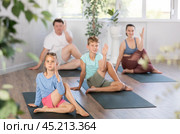 Little girl performs Lord of fish Ardha Matsyendrasana asana, family in background. Стоковое фото, фотограф Яков Филимонов / Фотобанк Лори