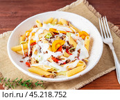 Penne pasta with yellow tomatoes, vegetables, mincemeat, white sauce on dark wooden background, side view, close up. Стоковое фото, фотограф Natalia Gdovskaia / Фотобанк Лори