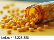 An orange plastic bottle of pills, from which bright yellow pills spilled out onto the table. The pills are laid out chaotically, creating a dynamic image. The bottle is translucent, allowing you to partially see the remaining pills inside. The light falls softly, emphasizing the texture of the pills and the glossy surface of the bottle. The background of the photo is neutral, which emphasizes the bright colors and creates a sense of cleanliness and order. This shot is ideal for illustrating themes related to medicine, health and pharmaceuticals. Стоковое AI-изображение, AI-художник Анна Кривицкая / Фотобанк Лори