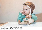A handsome little boy of 2 years old in a pilot's hat is playing with a wooden airplane and a logistics constructor. Children's wooden toys for child development. Стоковое фото, фотограф Photojuli / Фотобанк Лори
