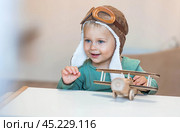 A handsome little boy of 2 years old in a pilot's hat is playing with a wooden airplane and a logistics constructor. Children's wooden toys for child development. Стоковое фото, фотограф Photojuli / Фотобанк Лори