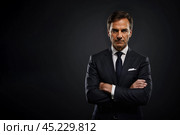 Successful businessman with crossed arms in magnificent suit stands on dark background. portrait of charismatic billionaire. Стоковое фото, фотограф Павел Муравьев / Фотобанк Лори