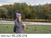 On a warm autumn day, a woman walks through the park. The girl is drinking coffee and talking on the phone. Стоковое фото, фотограф Photojuli / Фотобанк Лори