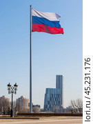 Флагшток с флагом России и современное высотное здание. Большой трёхцветный флаг развивается в небе. Москва, Россия (2023 год). Редакционное фото, фотограф Андрей Степанов / Фотобанк Лори