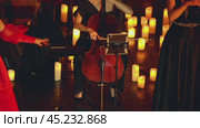 A close-up of a woman playing the cello. A group of women performing music on a dimly lit stage illuminated by numerous candles. They are all dressed in evening gowns. Стоковое видео, видеограф Воловодов Владимир / Фотобанк Лори