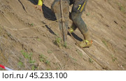The navigator of an off-road crew is climbing a steep slope. A man is pulling a winch anchor behind him. A close-up of the athlete's legs and anchor. Off-road racing. Стоковое видео, видеограф Воловодов Владимир / Фотобанк Лори
