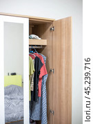 Wooden wardrobe with mirror and open door, clothes on hangers in the wardrobe. Стоковое фото, фотограф Коханова Наталья / Фотобанк Лори