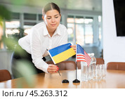 Female office coordinator placing flags of Ukraine and United States on table. Стоковое фото, фотограф Яков Филимонов / Фотобанк Лори
