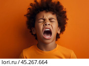 Extremely Upset black curly haired boy in t shirt screaming and crying with opened mouth and closed eyes against orange yellow color wall. Стоковое AI-изображение, AI-художник Sergey Grishin / Фотобанк Лори