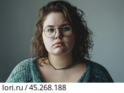 Ugly Young plus size woman wearing casual clothes and glasses sad expression on face with grey background. Apathy, depression, bulling, harassments concept. Social problem of fat people. Стоковое AI-изображение, AI-художник Sergey Grishin / Фотобанк Лори