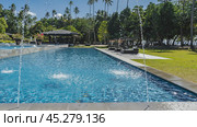 Outdoor swimming pool. Water jets around the perimeter. Ripples on the water, splashes. Sun beds with soft mattresses under awnings. Lush tropical vegetation, palm trees. The blue sky. Philippines. Стоковое фото, фотограф Вера Ивановна Кубарева / Фотобанк Лори