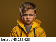 Portrait of disgruntled blond boy against yellow background. The boy experiencing negative emotions due to fact that his family tore him away from computer games and forced him. Sulking Caucasian boy. Стоковое AI-изображение, AI-художник Sergey Grishin / Фотобанк Лори