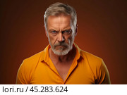 Despise. Angry and grumy Caucasian gray-haired bearded man sulking, furrow eyebrows and staring with anger and contempt, boiling from furious emotions, standing over red background. Стоковое AI-изображение, AI-художник Sergey Grishin / Фотобанк Лори