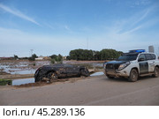 The aftermath of hurricane Dana in Valencia, Spain - Muddy car damaged by floodwaters in Valencia, Spain, with police vehicle attending the scene. Редакционное фото, фотограф Данил Руденко / Фотобанк Лори