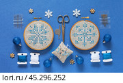 Merry Christmas and Happy New Year. Close-up of hand embroidered snowflakes in cross stitch on blue background. Winter handcraft and Christmas gifts concept. Cross stitch as a hobby. Flat lay, top view. Стоковое фото, фотограф Виктория Катьянова / Фотобанк Лори