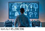 Healthcare worker in dimly lit room examines detailed MRI scans, images of human anatomy displayed on large, advanced monitor showcasing brain and chest area. Стоковое AI-изображение, AI-художник Павел Муравьев / Фотобанк Лори