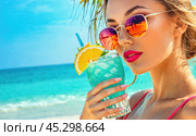 Young woman in sunglasses enjoys cocktail by beach, smiling under sky. azure ocean waves in backdrop. relaxation and vacation, tropical paradise setting, leisure travel escape. Стоковое AI-изображение, AI-художник Павел Муравьев / Фотобанк Лори