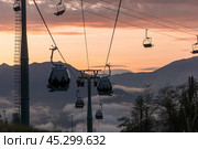 Ski gondolas glide above misty mountains at sunset, offering stunning views of the vibrant sky and surrounding landscape. Стоковое фото, фотограф Алексей Климкин / Фотобанк Лори
